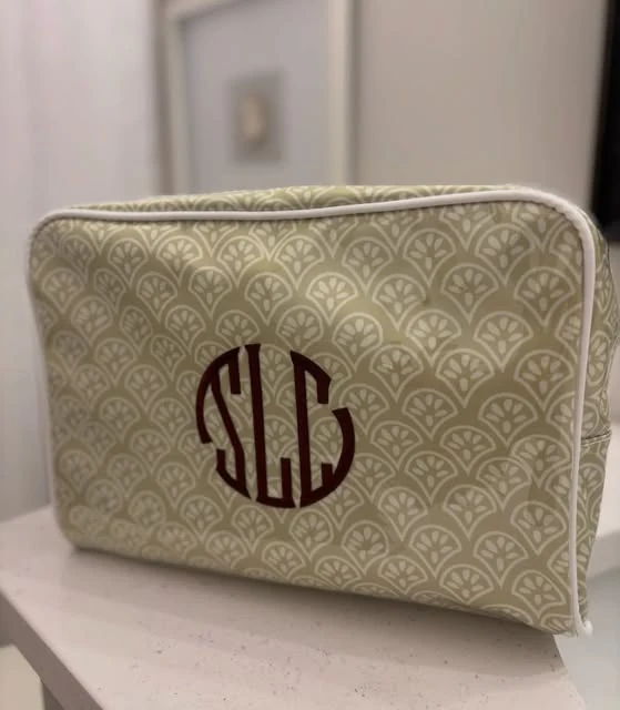 An olive and cream fan-pattern cosmetic pouch with a burgundy monogram reading SLC